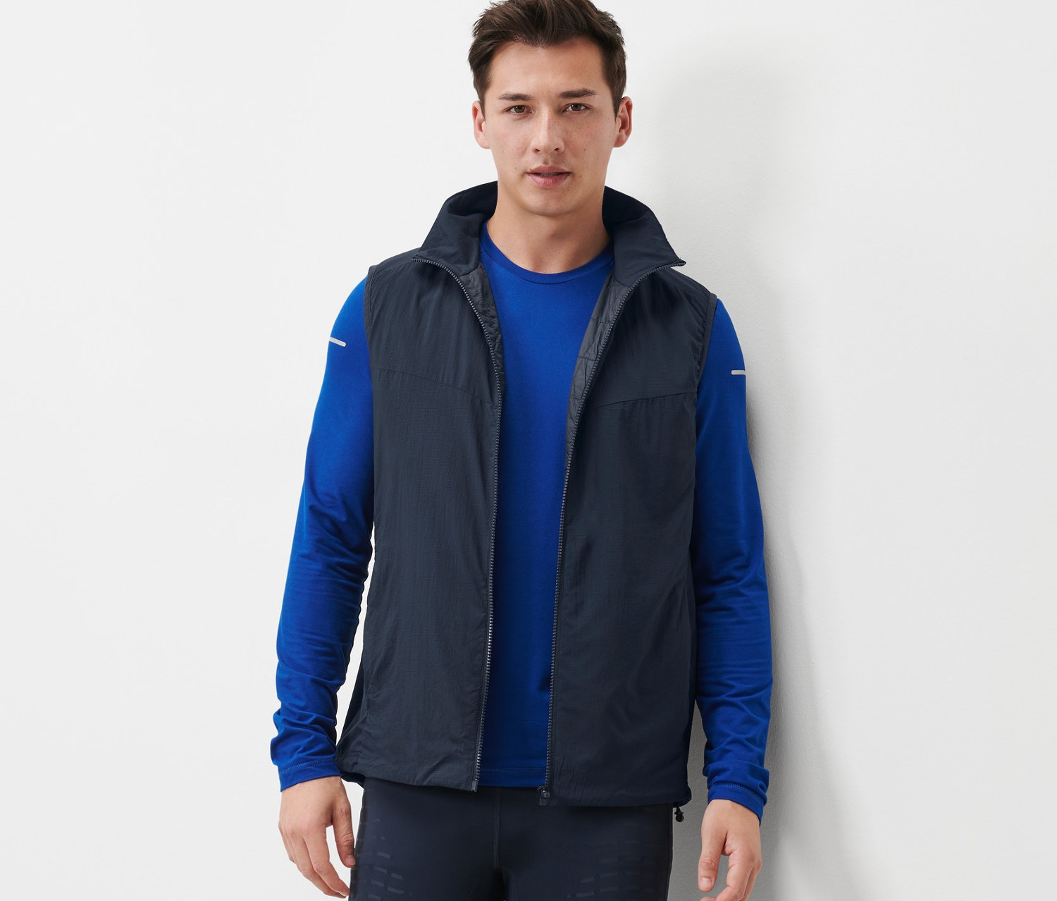 Férfi funkcionális mellényt, kék hosszú ujjú inget és sötét leggingset visel.