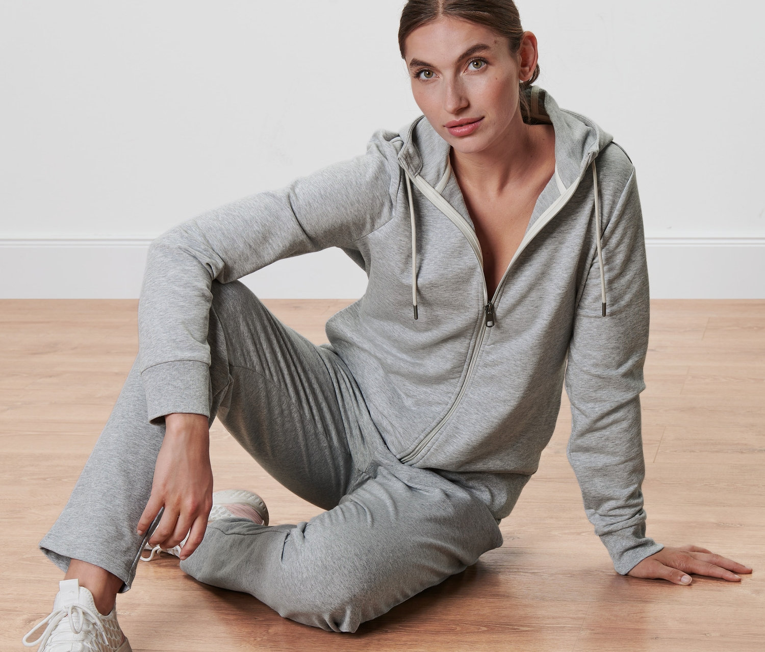 Nő ül a padlón, szürke kapucnis szabadidőfelsőt visel.