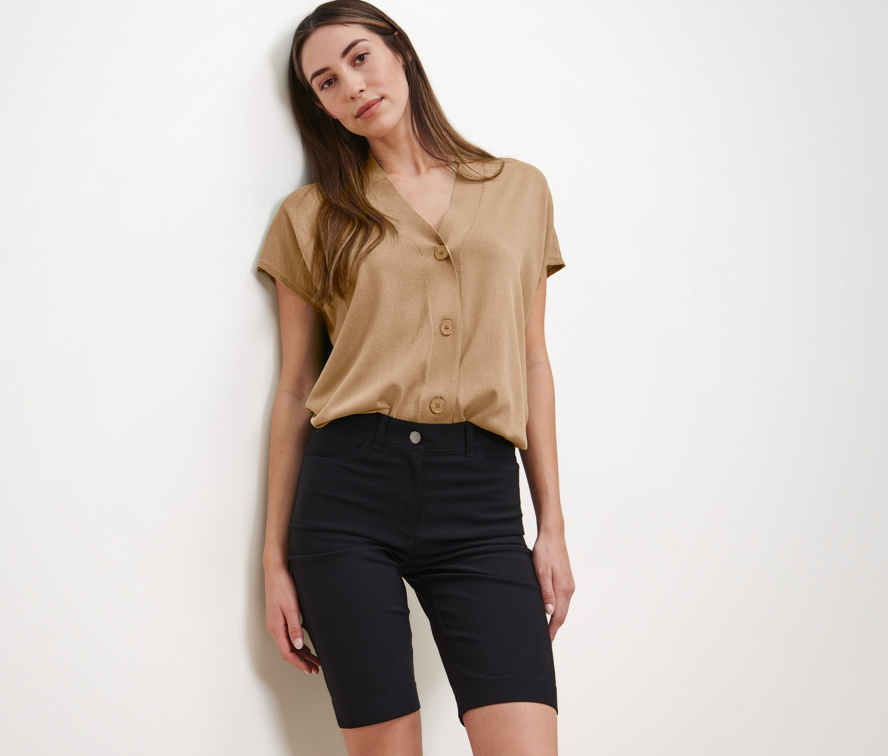 Nő pózol bézs blúzban és fekete bengalin bermudanadrágban.