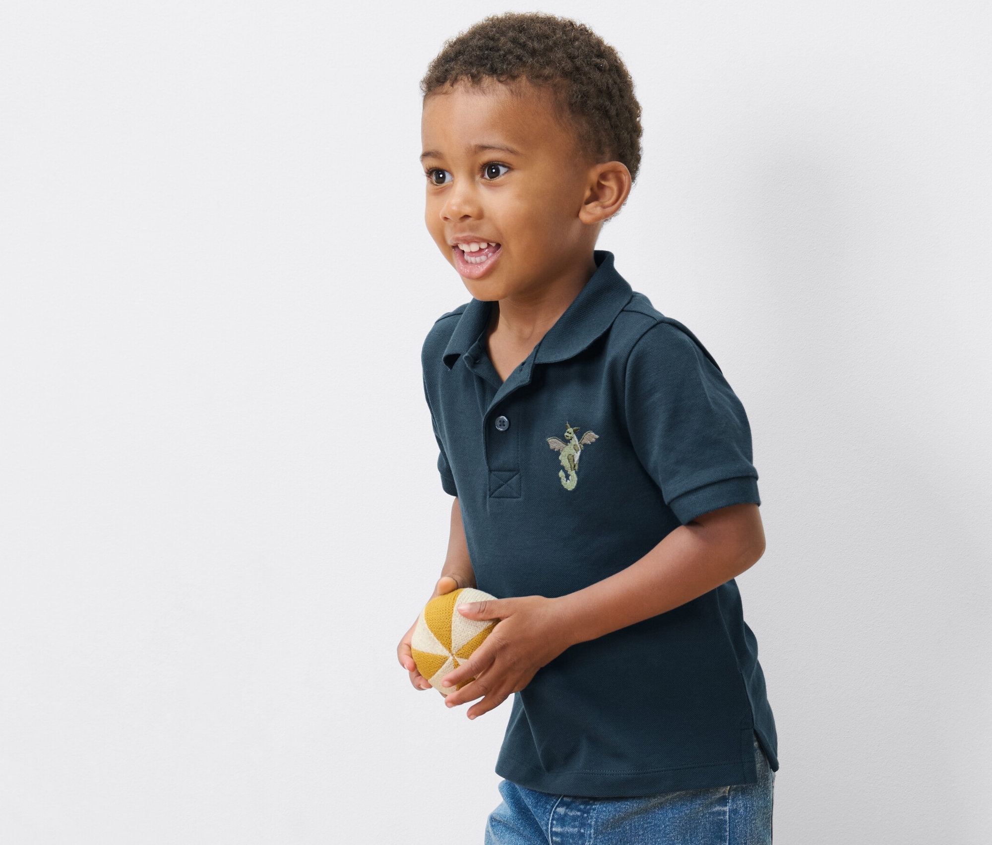 Fiú visel egyet a 2 gyerek pólóing pamut piké anyagból származó termékből, és egy labdát tart.