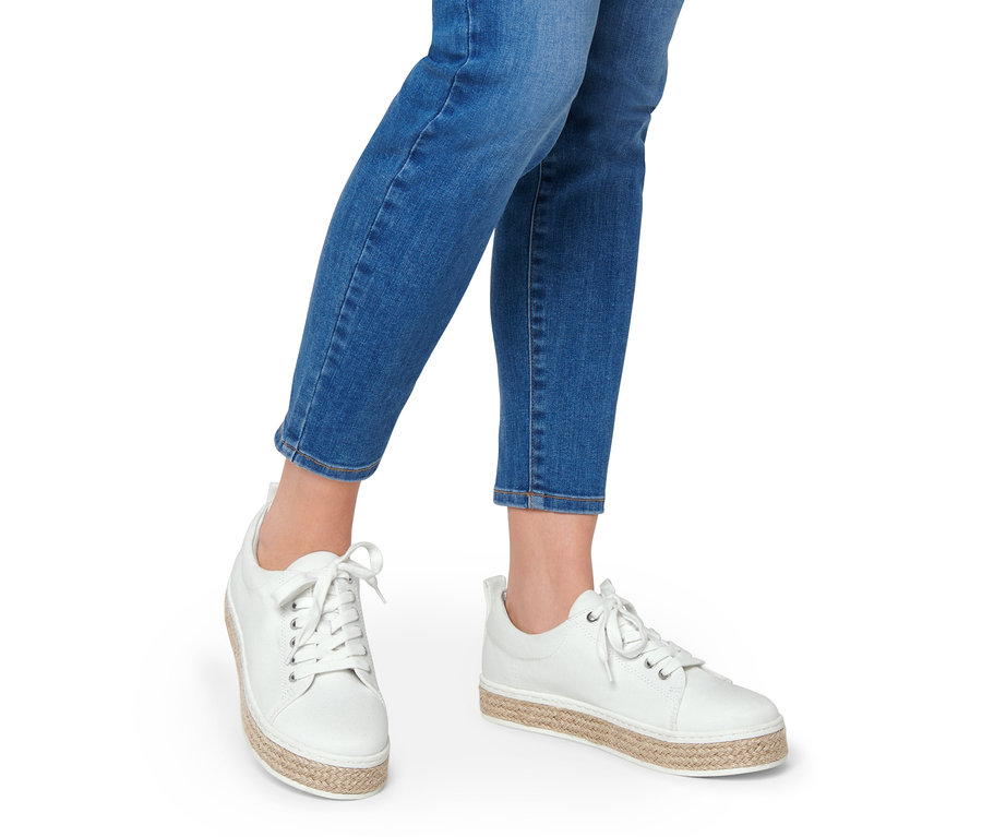Egy nő lábai farmerban és fehér vászon sneaker cipőben.
