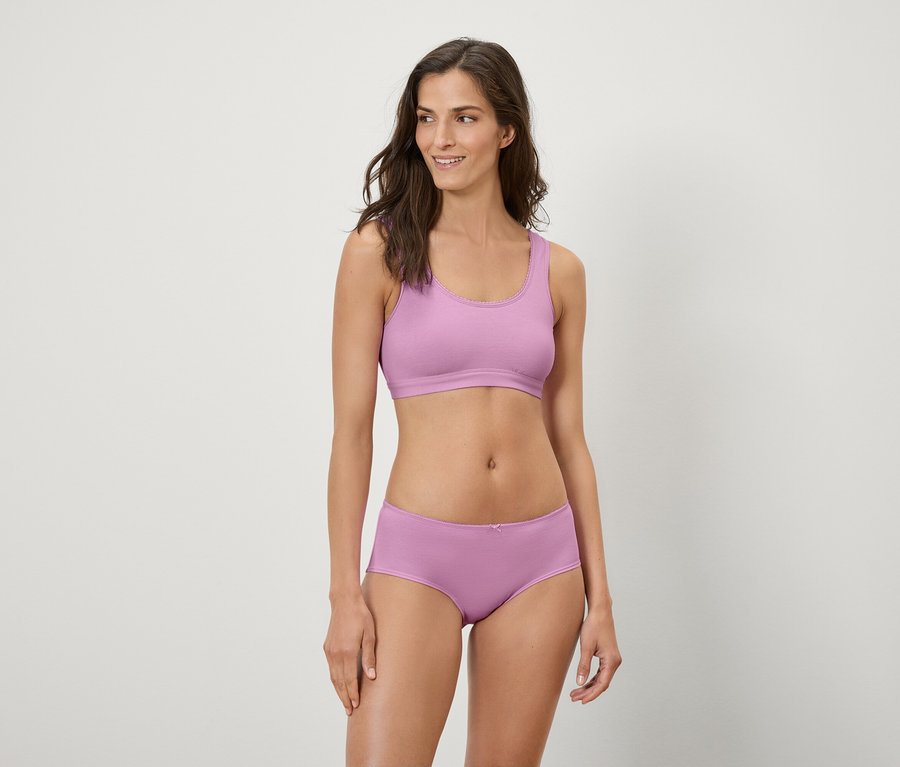 Nő lila sportmelltartóban és boxeralsóban pózol.