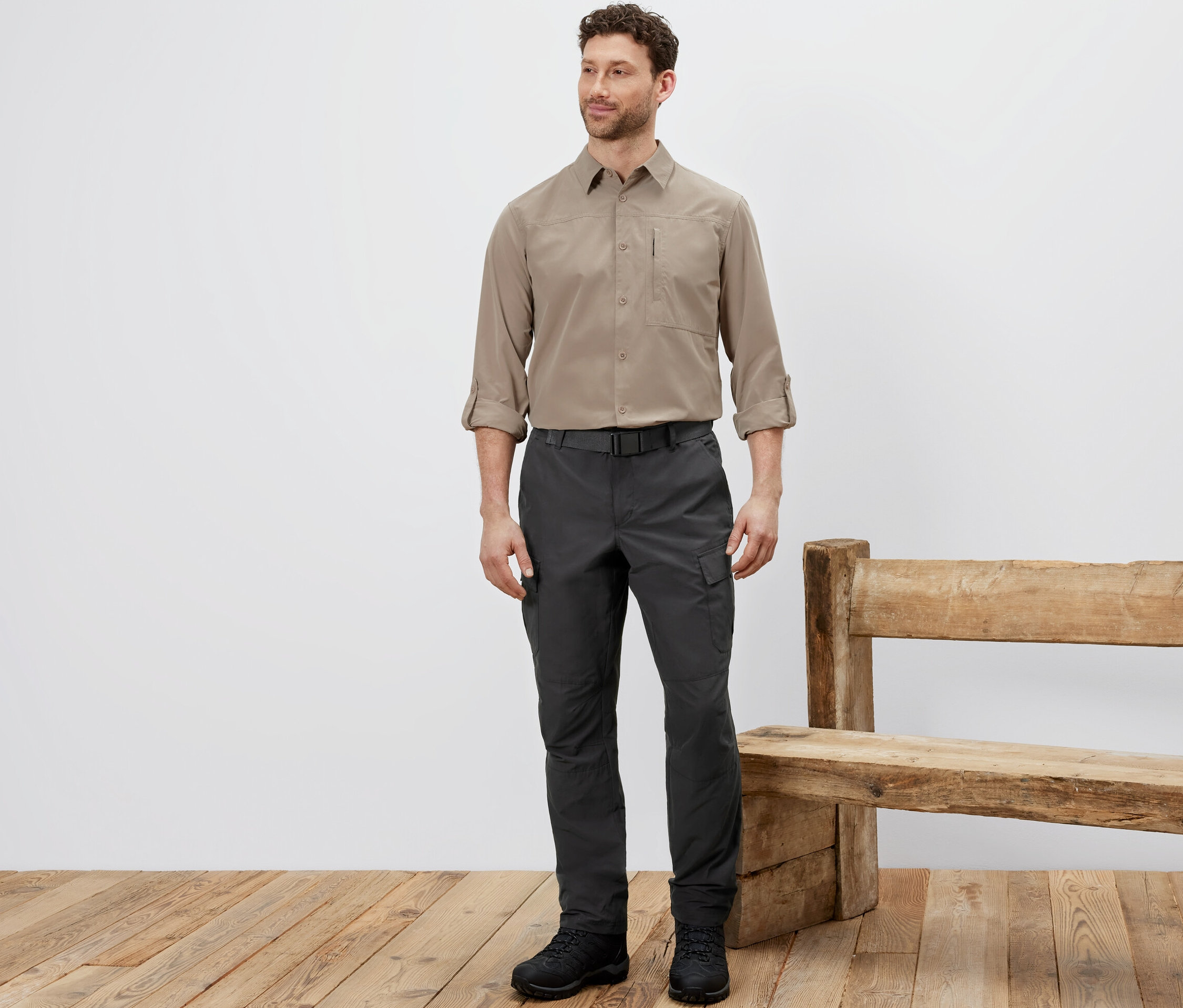 Férfi áll szúnyogok elleni védelemmel ellátott túranadrágban, bézs ingben és fekete cipőben.