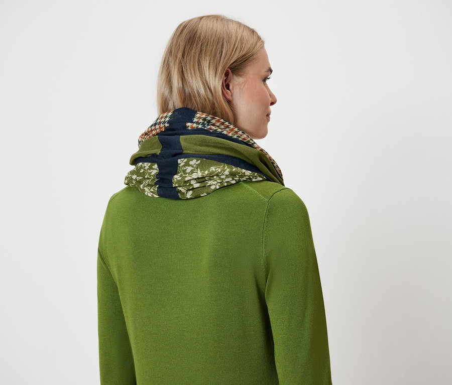 Egy szőke hajú nő zöld pulóverben és sálban hátulról.