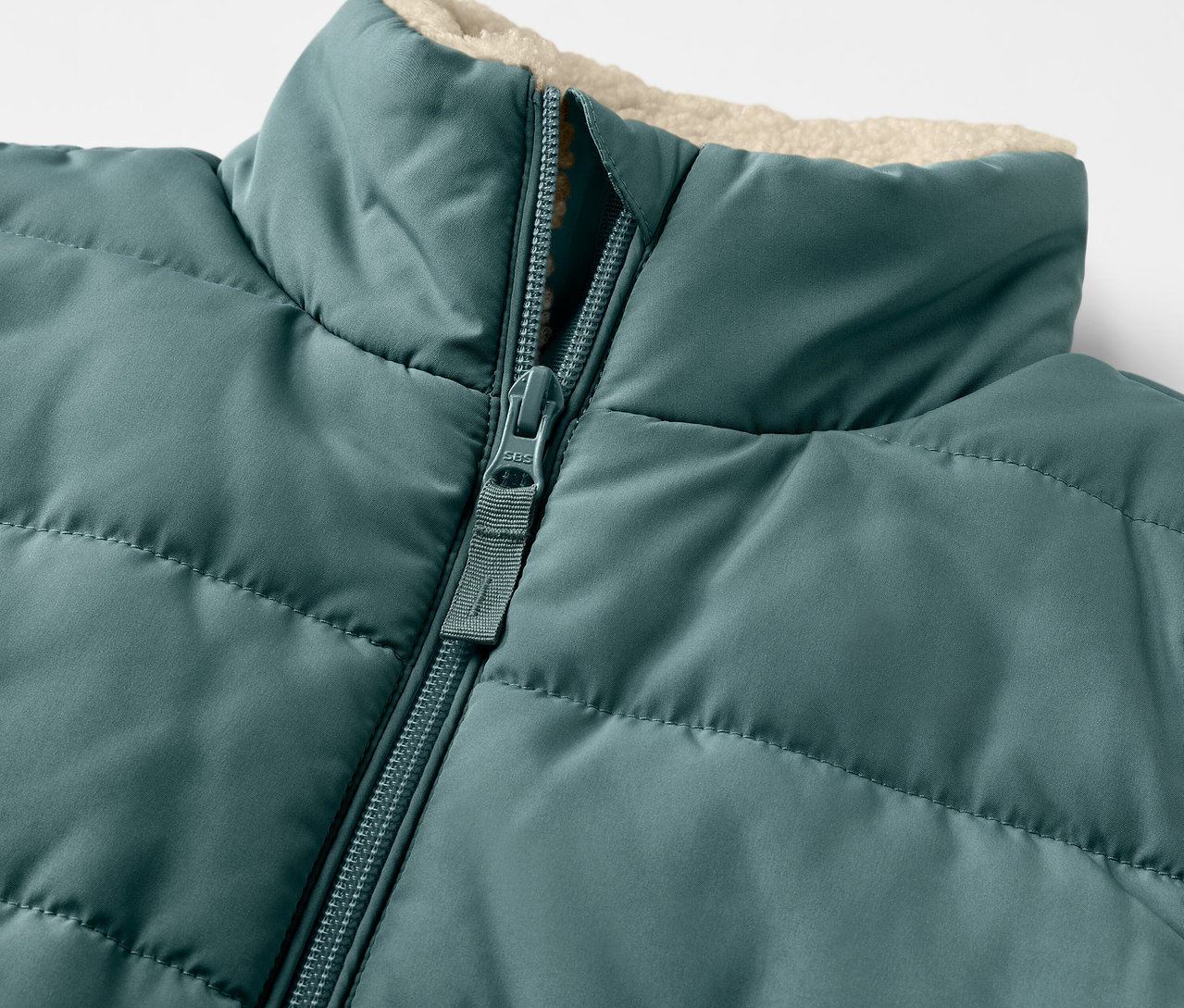 Egy plüss, steppelt gyerekmellény részlete, cipzárral.