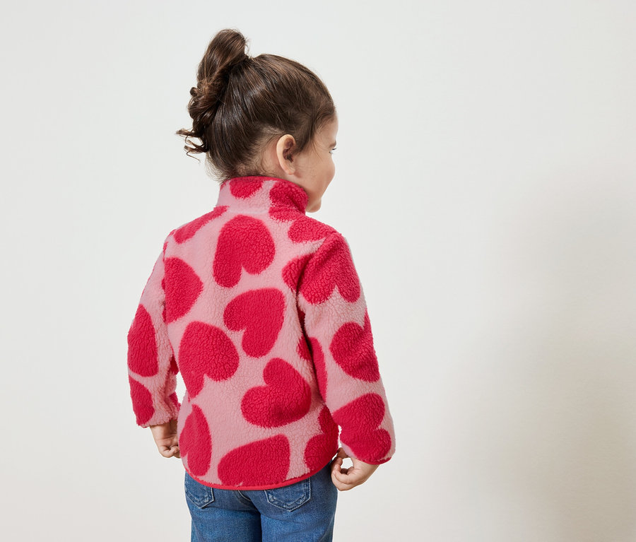 Kislány piros szíves pulóverben, jobbra néz.