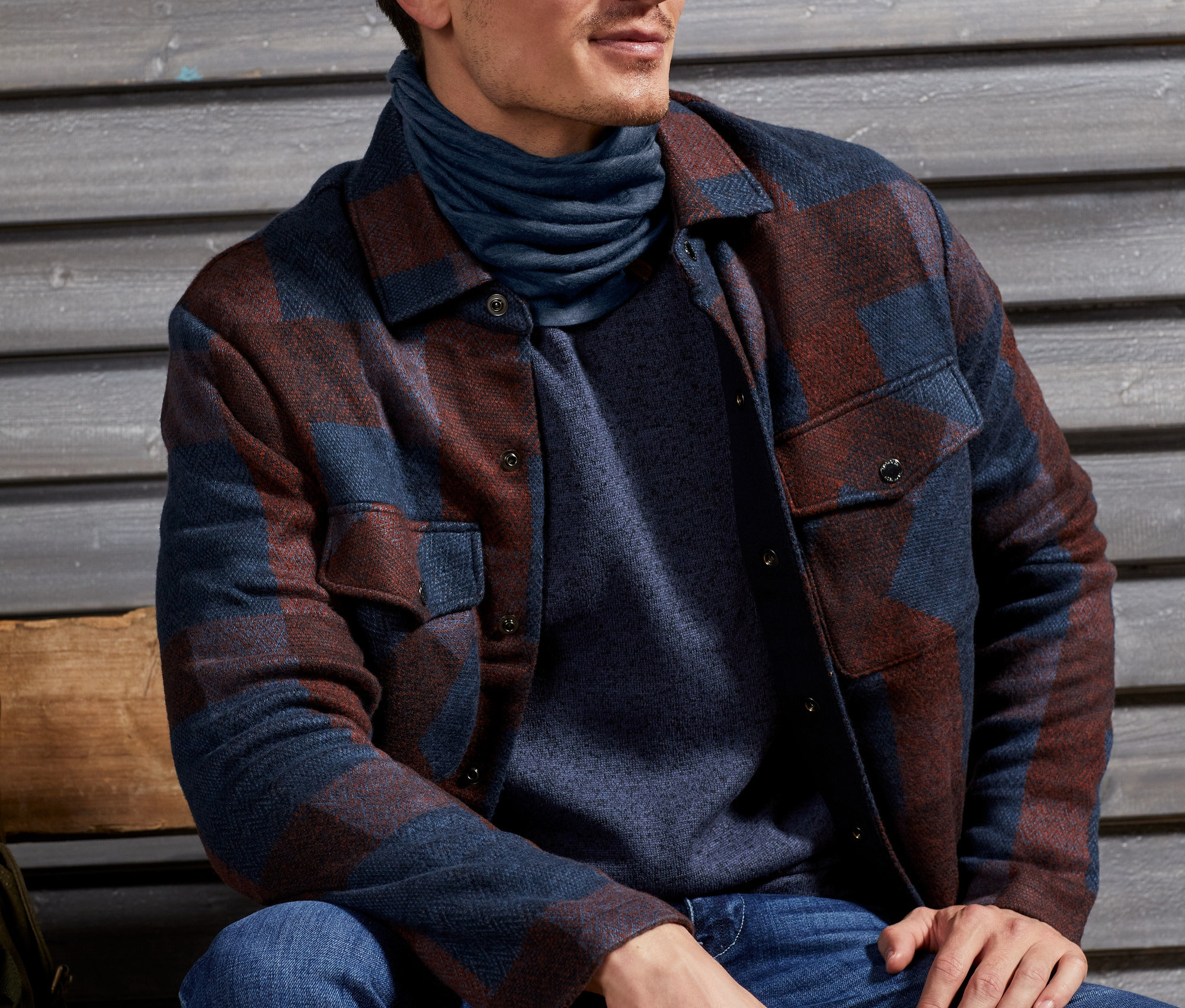 Férfi ül, sötétkék merinógyapjú multifunkcionális kendőt és kockás férfi ingkabátot visel.