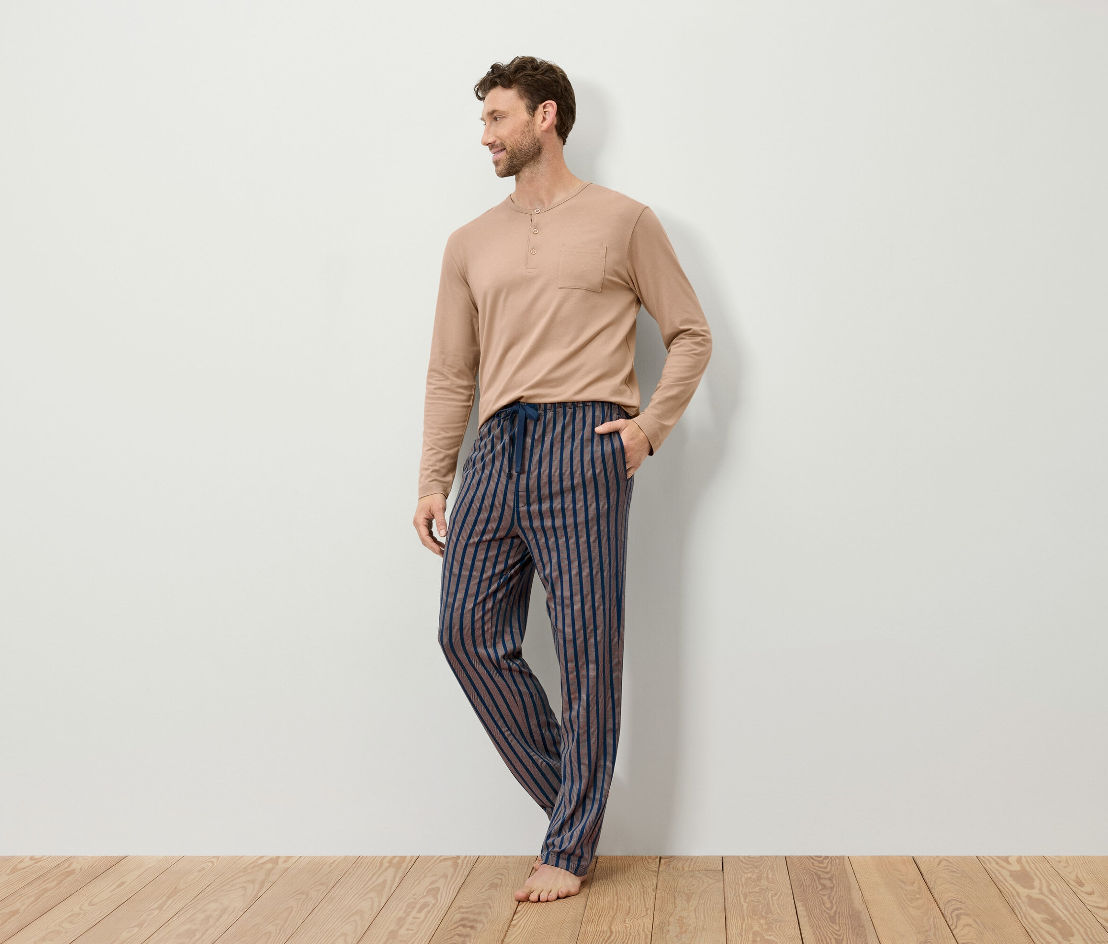 Férfi bézs színű, hosszú ujjú pizsama felsőben és csíkos pizsama nadrágban.