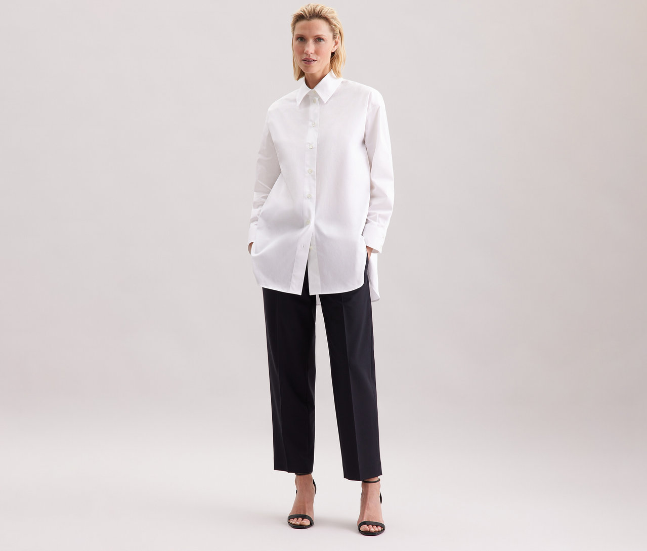 Nő fehér Seidensticker túlméretes hosszú ingblúzban és fekete nadrágban.