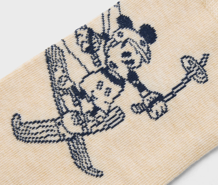 Egy bézs színű zokni részlete, sötétkék síelő Mickey egér mintával.