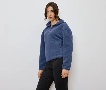 Nő pózol kék, kapucnis fleece pulóverben és fekete nadrágban.