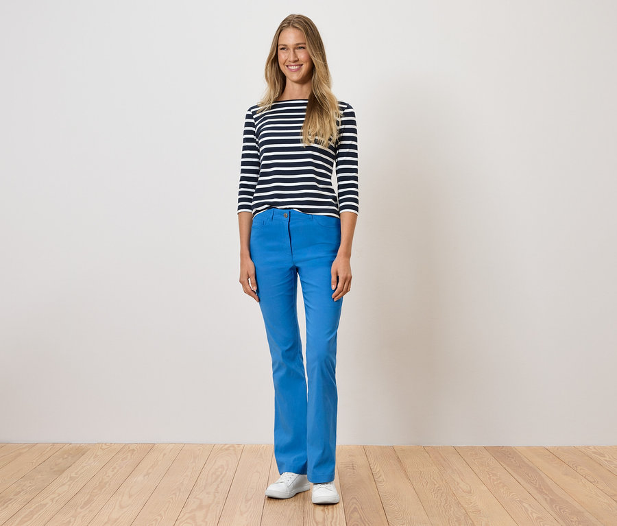Egy nő áll kék nadrágban, csíkos pólóban és fehér cipőben.