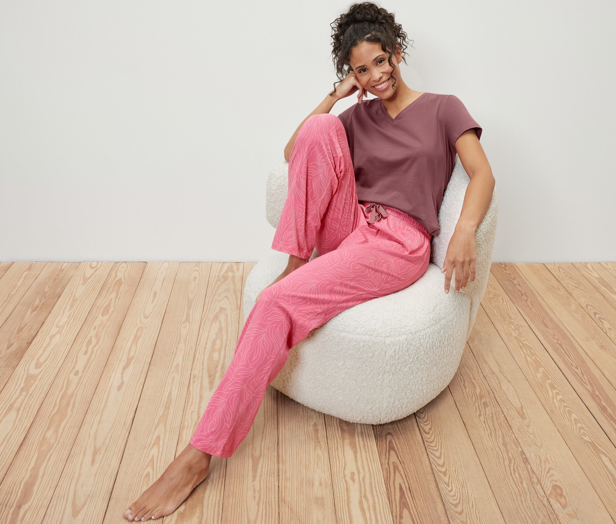 Nő ül egy fotelben, és rózsaszín/barna, levélmintás női pizsama van rajta.