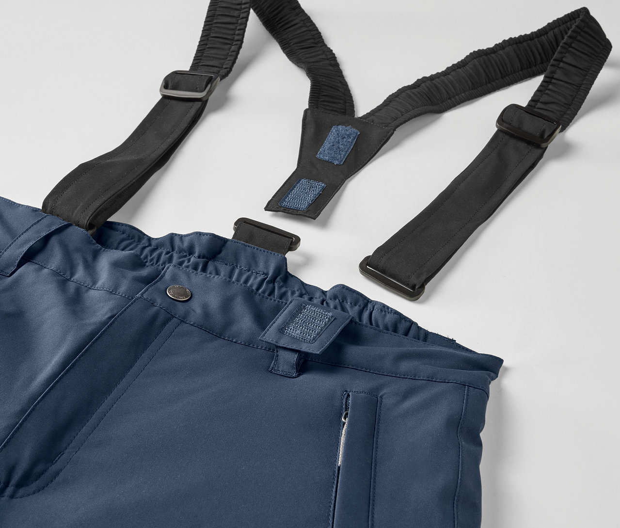 Kék nadrág részlete fekete, rugalmas nadrágtartókkal.