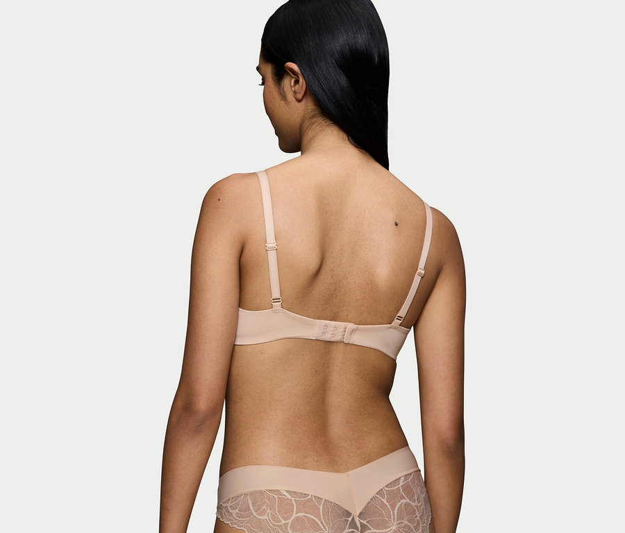 Hátulnézet egy fekete hajú nőről, aki testszínű melltartót és csipkés alsóneműt visel.