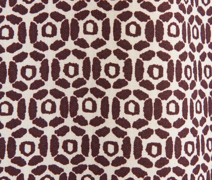 Egy barna geometrikus mintával díszített szövet közeli képe bézs háttéren.