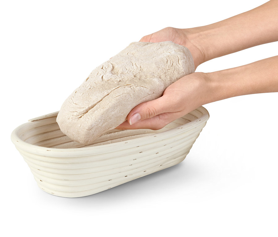 Két kéz egy kenyértésztát helyez egy kelesztő kosárba.