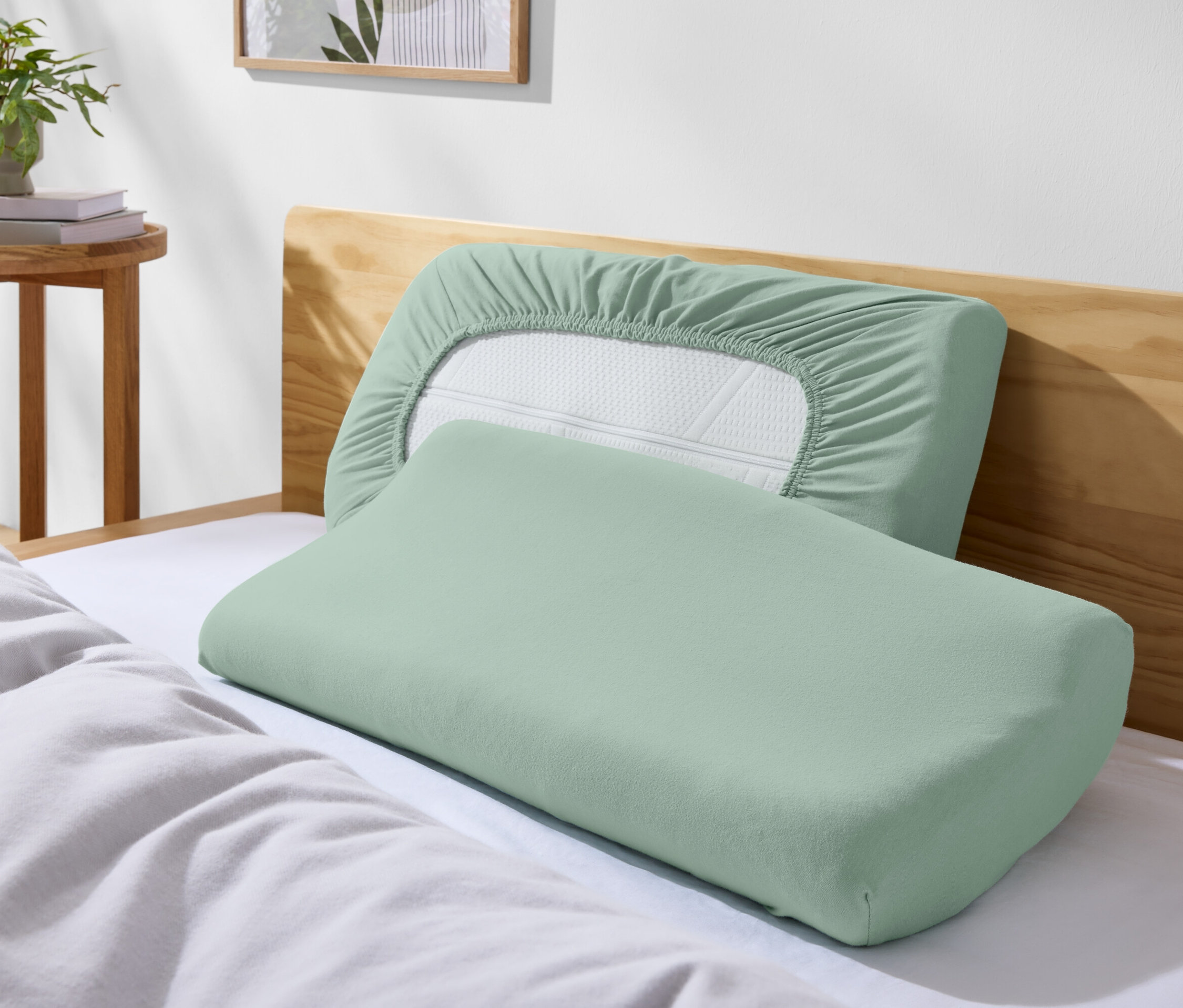 Két zöld párna egy ágyon fehér ágyneművel.