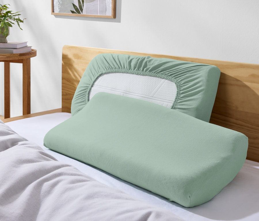 Két zöld párna egy ágyon fehér ágyneművel.