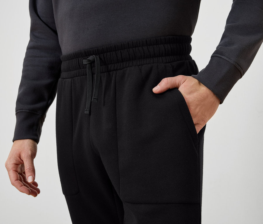 Férfi a kezét a fekete melegítőnadrág zsebében tartja.