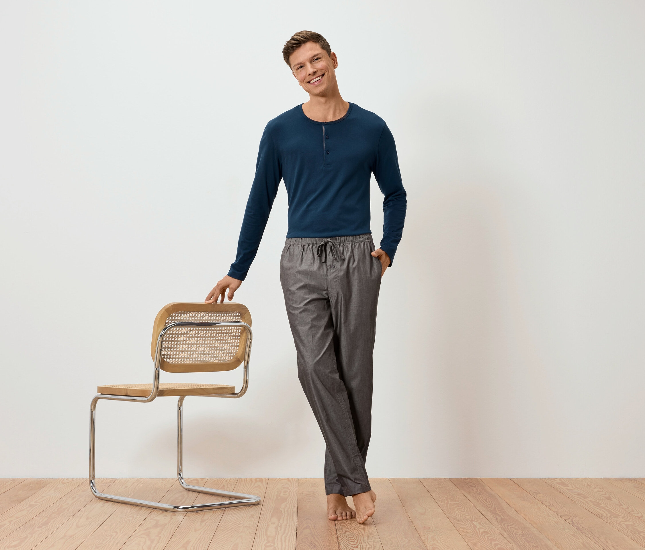 Egy férfi egy szék mellett pózol, szövött nadrágos pizsamát visel.