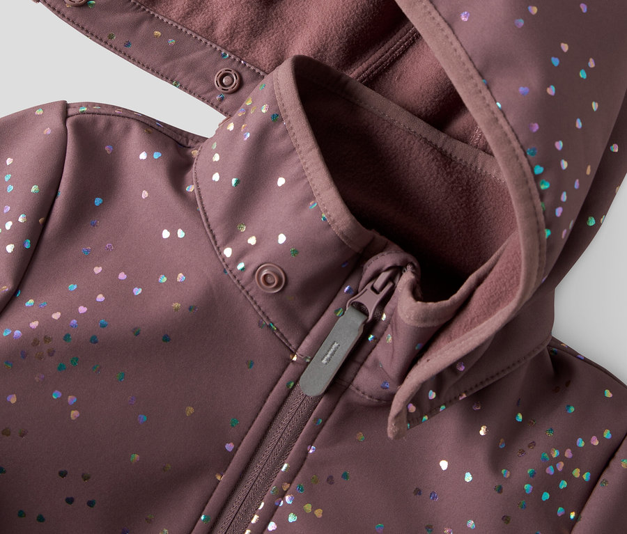Egy lila softshell kabát közeli képe kapucnival és cipzárral, színes szív alakú pöttyökkel díszítve.