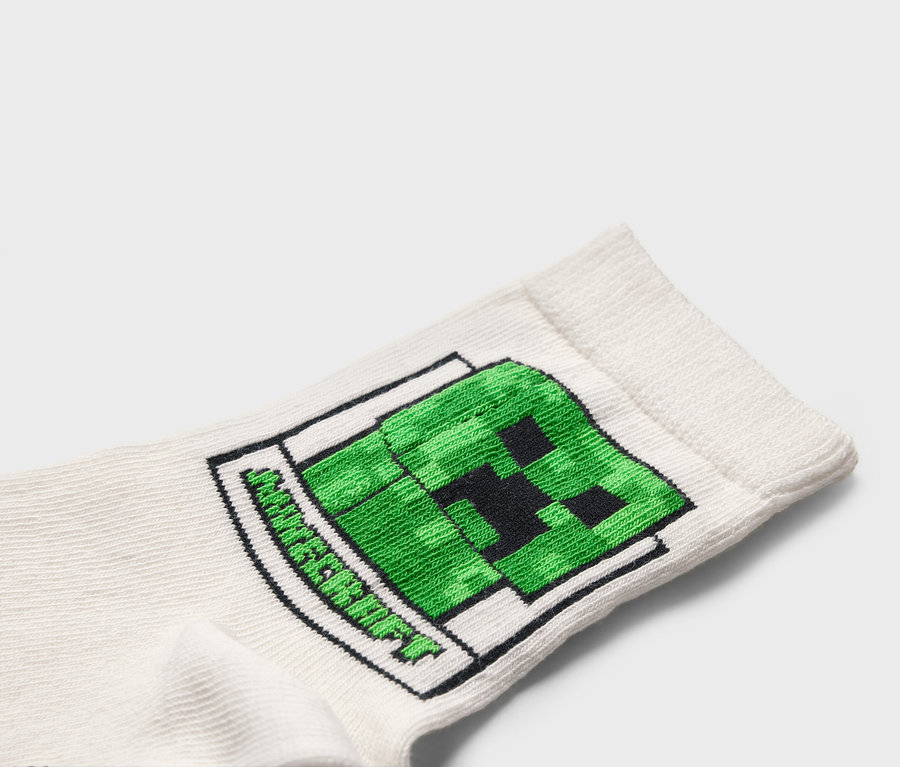 Egy fehér zokni közeli képe zöld Minecraft Creeper mintával.