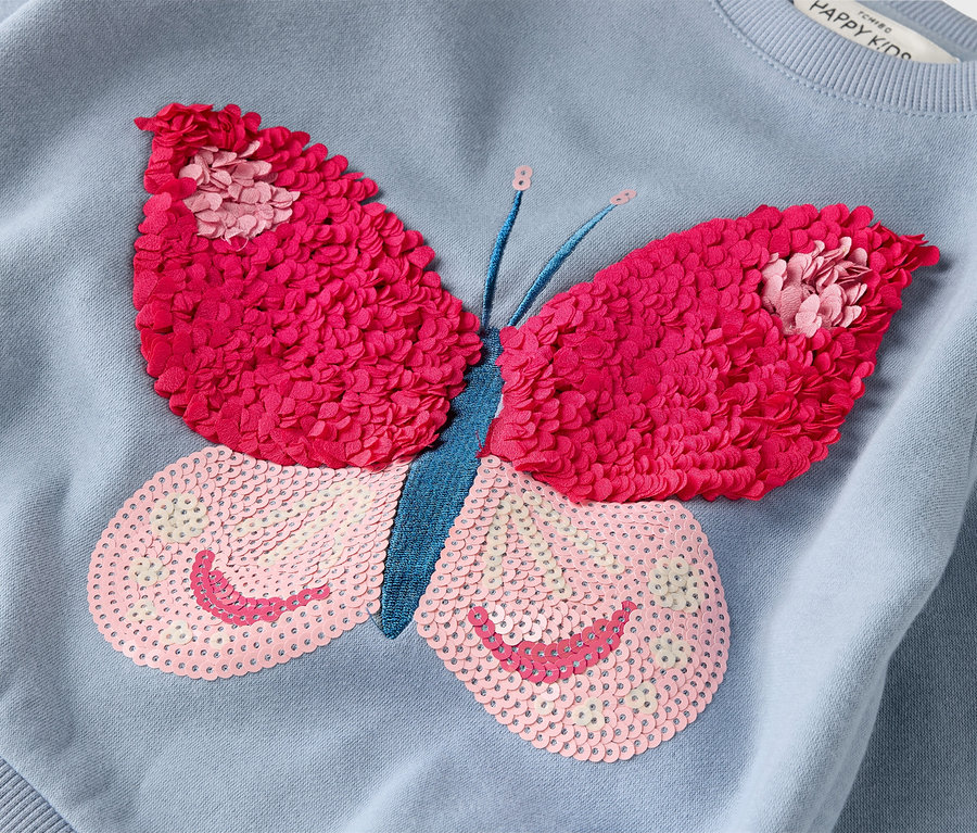 Közeli kép egy világoskék pulóverről, nagy, rózsaszín és pink pillangó rátéttel.