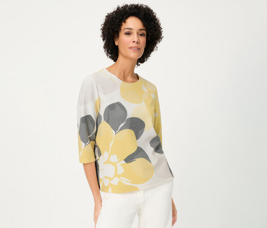 Nő visel egy Olsen »Ottoman« szabadidőfelsőt sárga és szürke virágokkal, fehér háttér előtt.