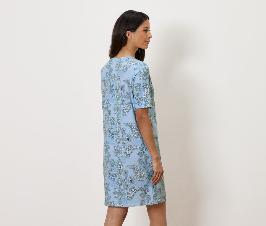 Nő áll oldalt, világoskék virágos ruhát visel.