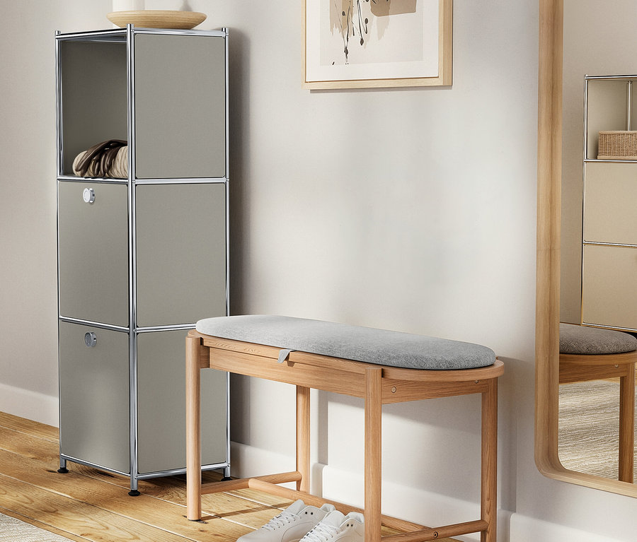 Szürke szekrény dekorációkkal egy szürke kárpitozott fa pad és fehér cipők mellett.