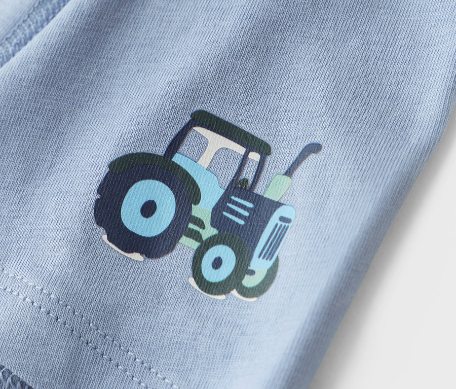 Közeli kép egy világoskék anyagról, traktor mintával.