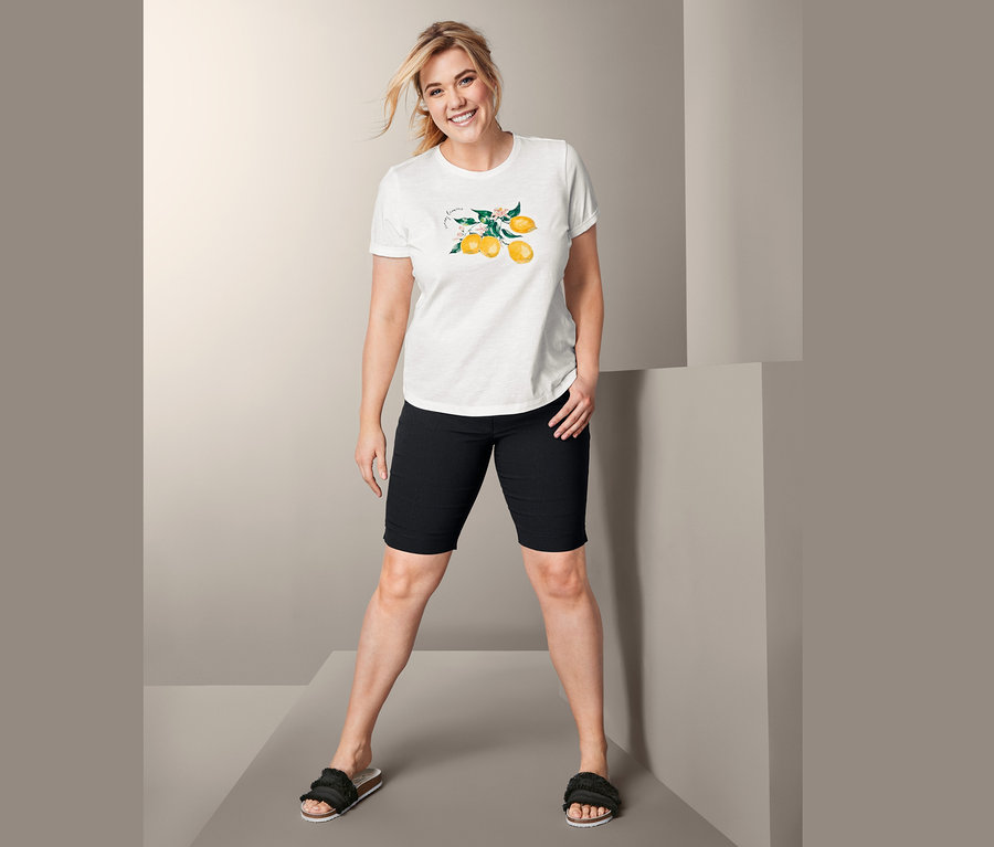 Nő pózol citrom mintás rövid ujjú trikóban, fekete rövidnadrágban és papucsban.