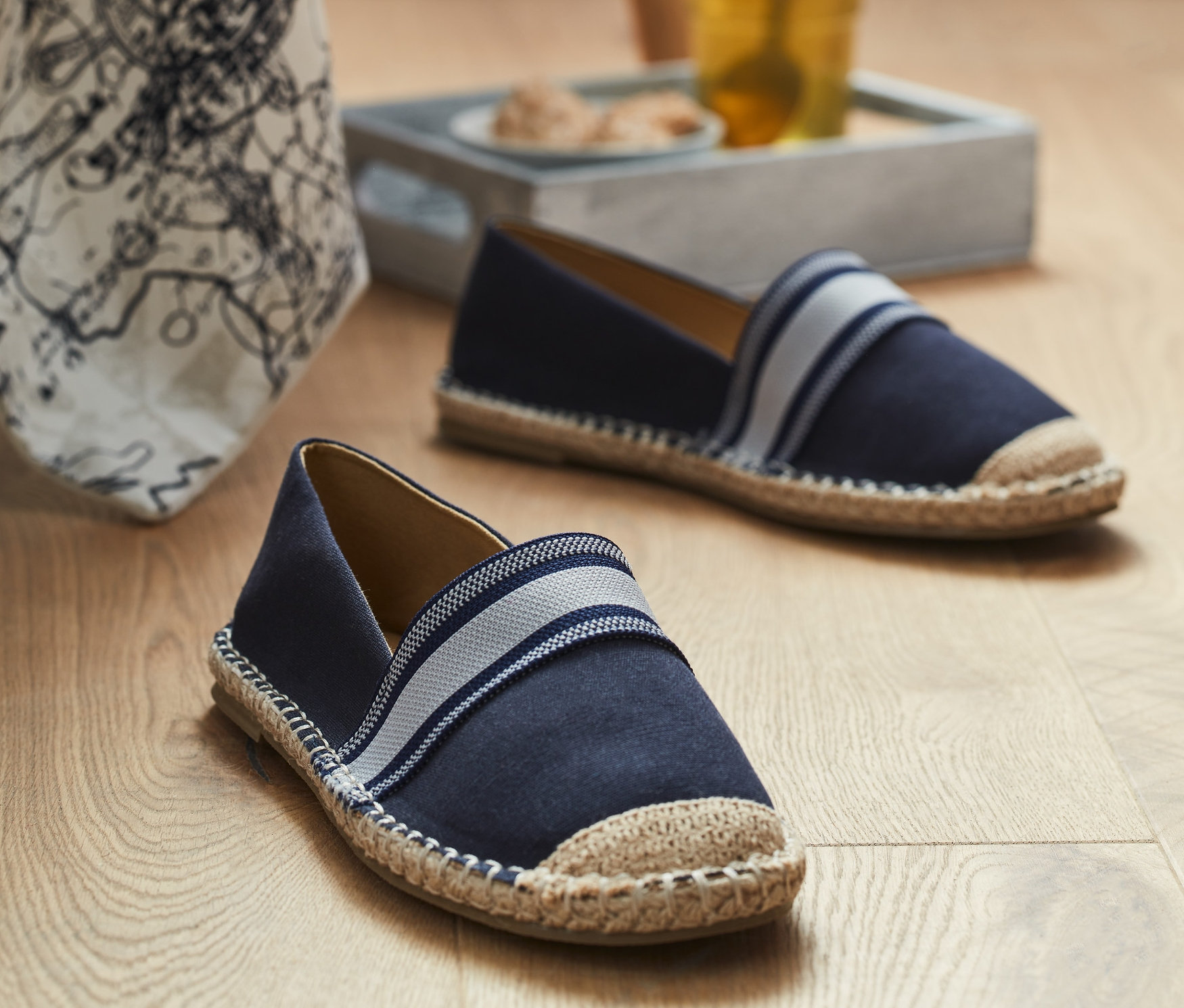 Két espadrilles a fapadlón egy pohár ital közelében.