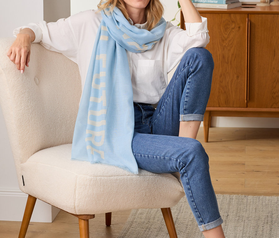 Nő ül a fotelben, világoskék, feliratos szövetsálat visel.