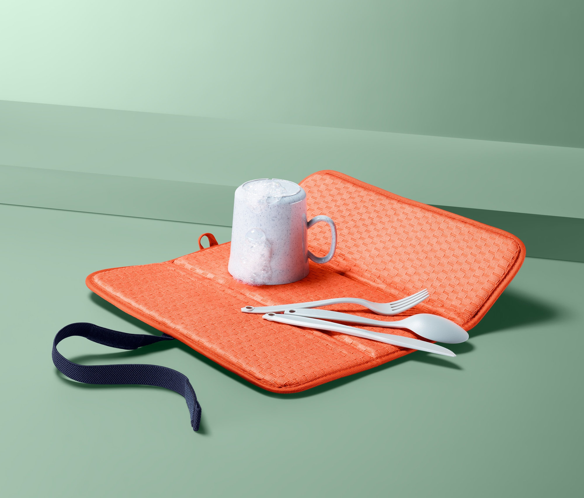 Pohár, kés, villa és kanál egy narancssárga összehajtható edénycsepegtető alátéten.