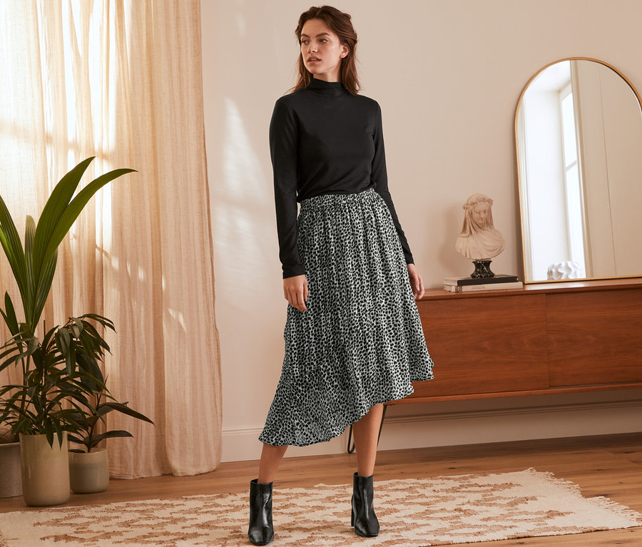 Nő pózol fekete garbóban és aszimmetrikus, állatmintás szoknyában.