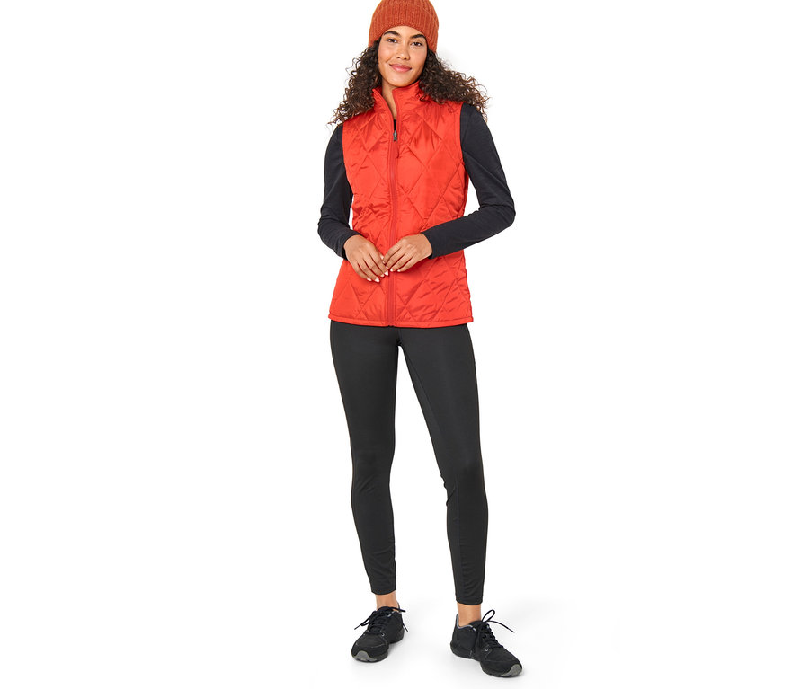 Nő visel egy narancssárga 3 az 1-ben esőkabátot, mellényt és egy barna sapkát.