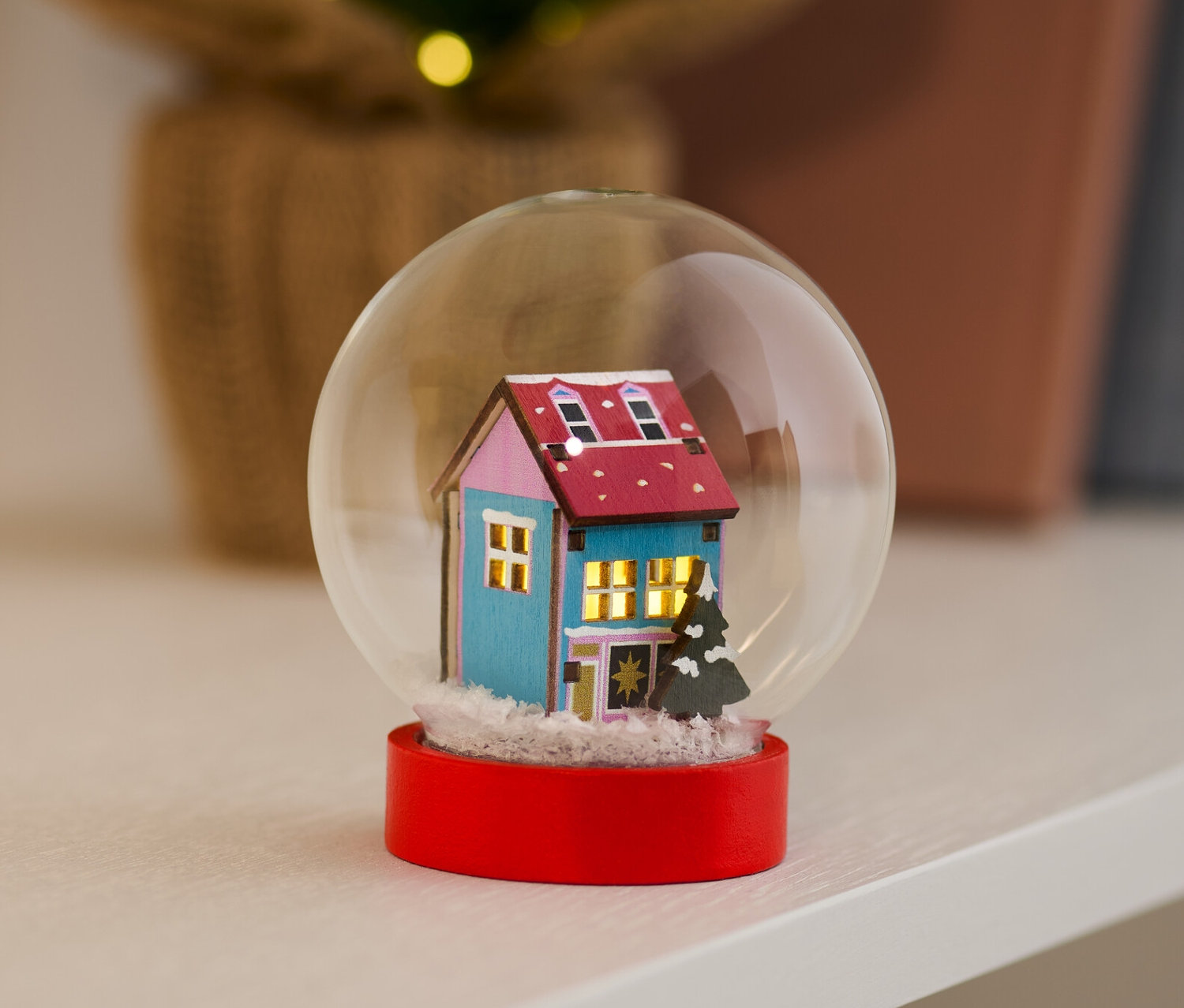 LED-es hógömb kék házzal és piros alappal egy polcon.