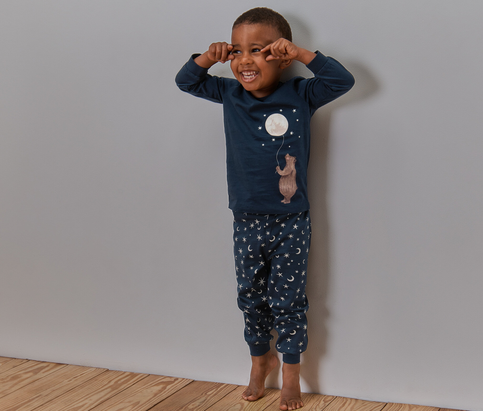 Egy fiú nevet és a fal mellett áll a Gyerekpizsamában (hold, világít a sötétben).