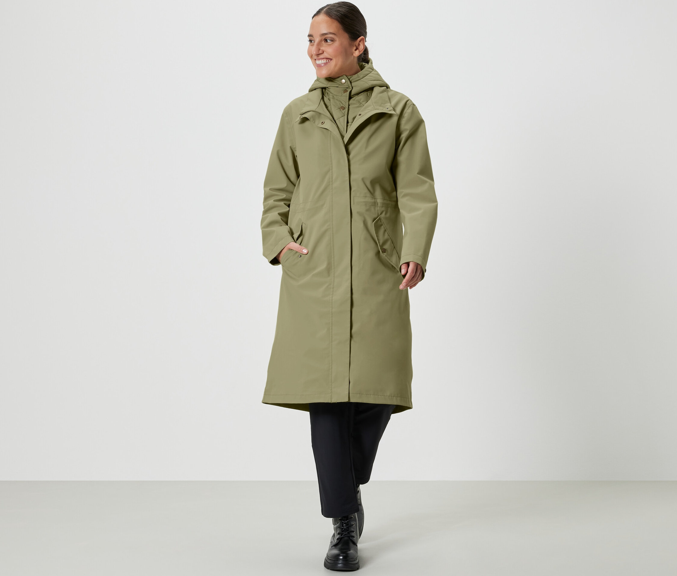 Nő sétál, khaki színű, levehető kapucnis esőkabátot visel.