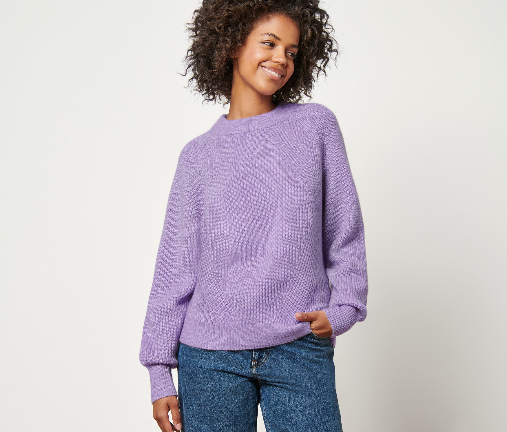 Nő kötött pulóverben és farmerban pózol.