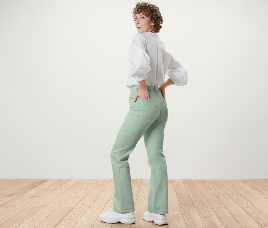 Nő néz a válla fölött, és mentazöld Bootcut »Lou« farmerban és fehér blúzban pózol.