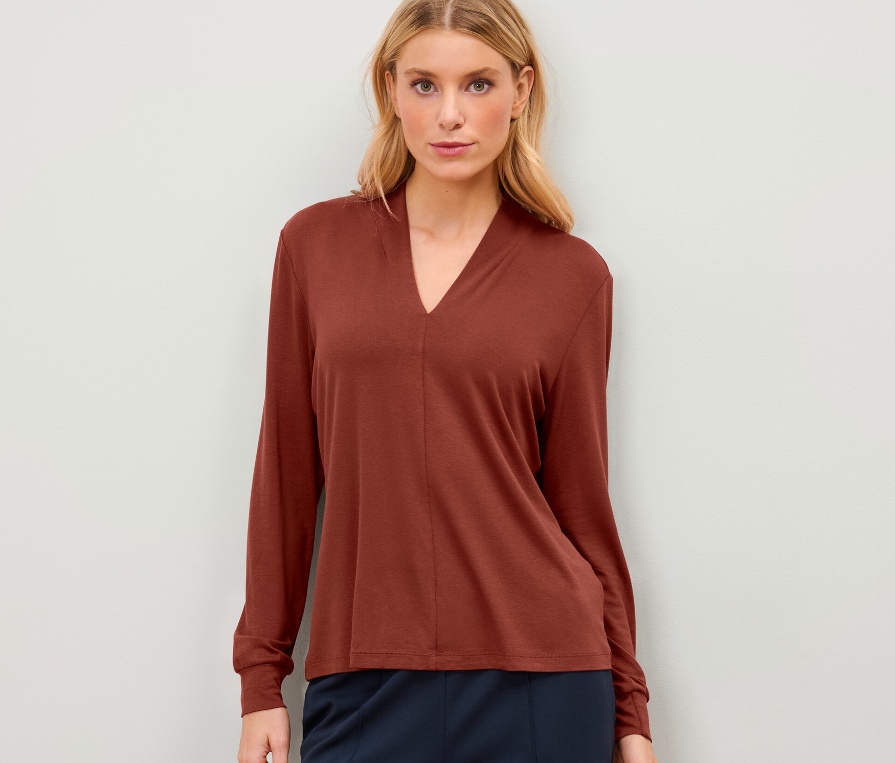 Nő visel egy rozsdabarna V-nyakú pólóblúzt.
