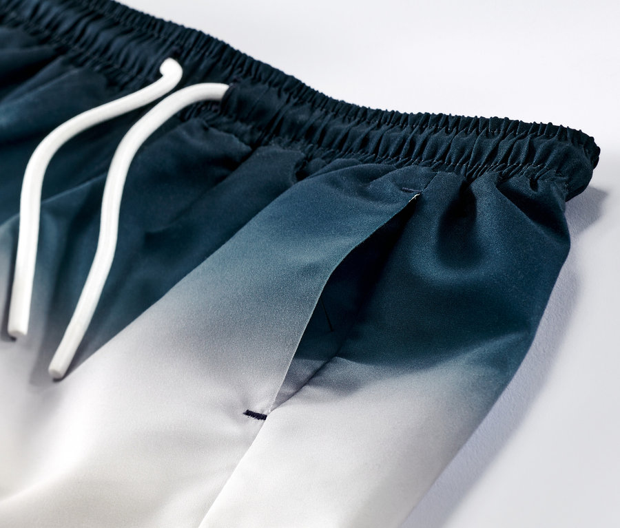 Egy fiú fürdőnadrág részlete, kék-fehér színátmenettel és fehér zsinórral.