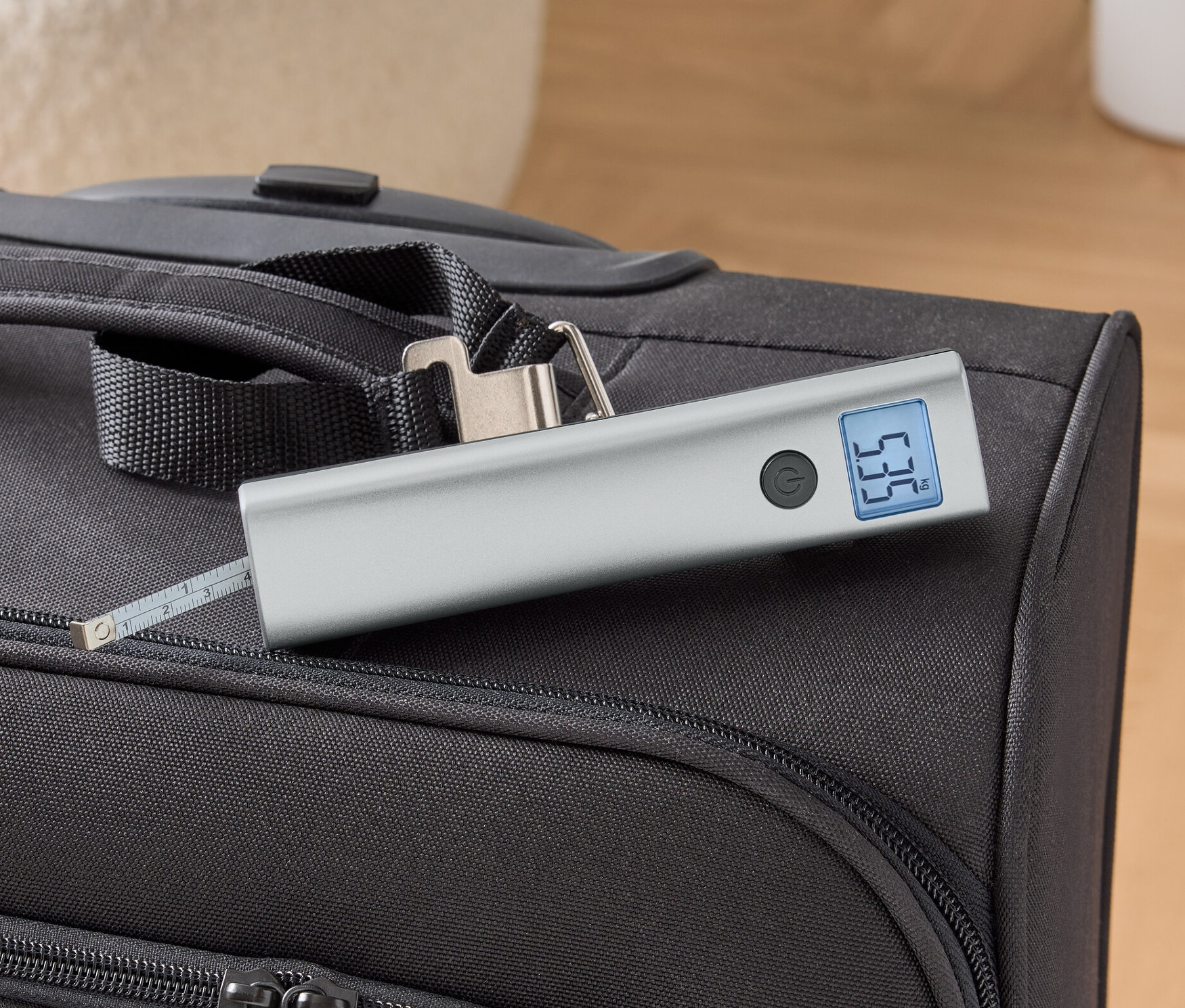 Digitális poggyászmérleg fekszik egy fekete bőröndön.