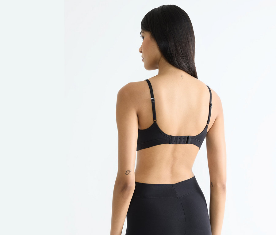 Hátulnézet egy hosszú hajú nőről, aki fekete melltartót és fekete leggingset visel.