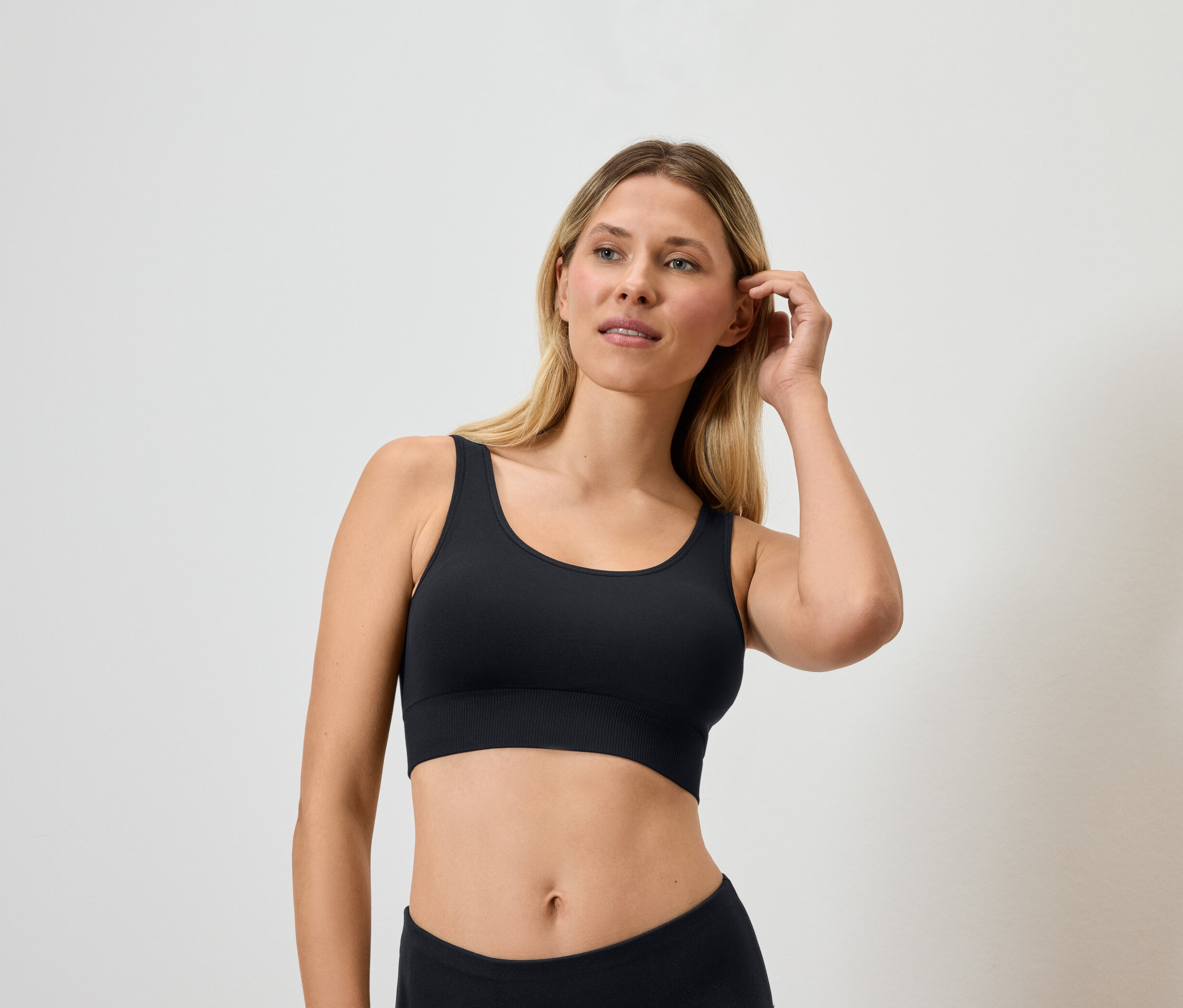 Szőke nő fekete sportmelltartót visel, és a haját érinti.