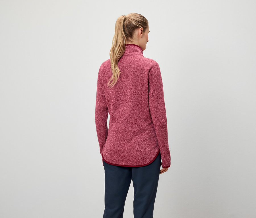 Hátulról látható egy szőke hajú, lófarokba kötött nő, aki piros pulóvert és sötétkék nadrágot visel.