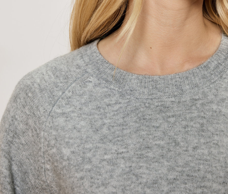 Egy női szürke pulóver részlete kerek nyakkivágással.